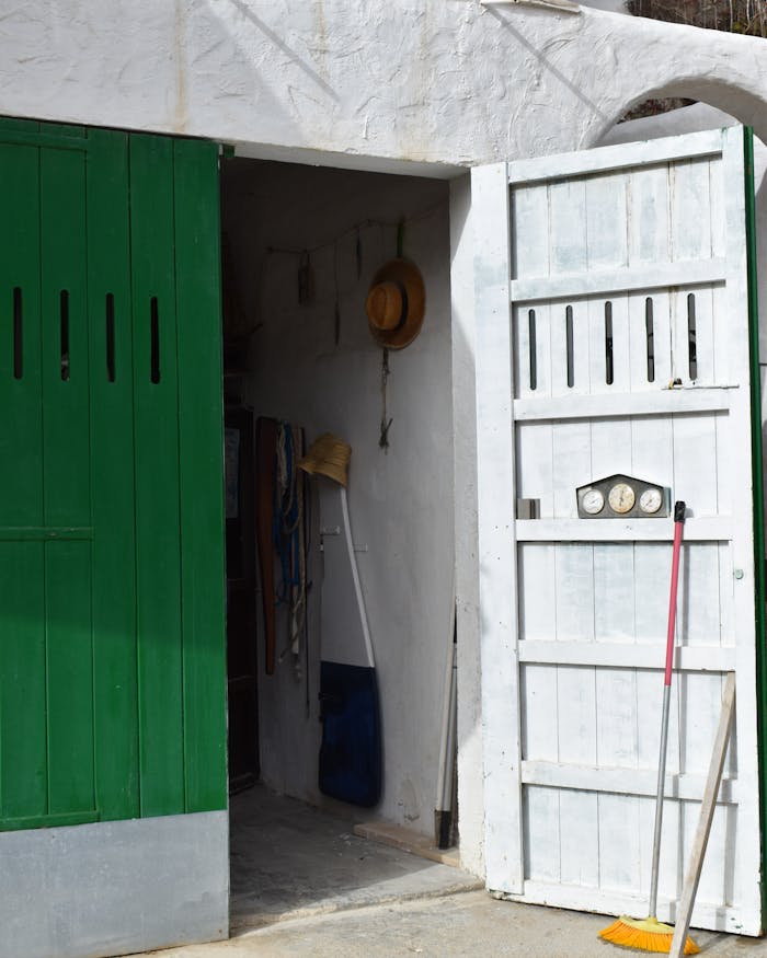 Charming old house entrance featuring green and white painted doors with cleaning tools nearby.